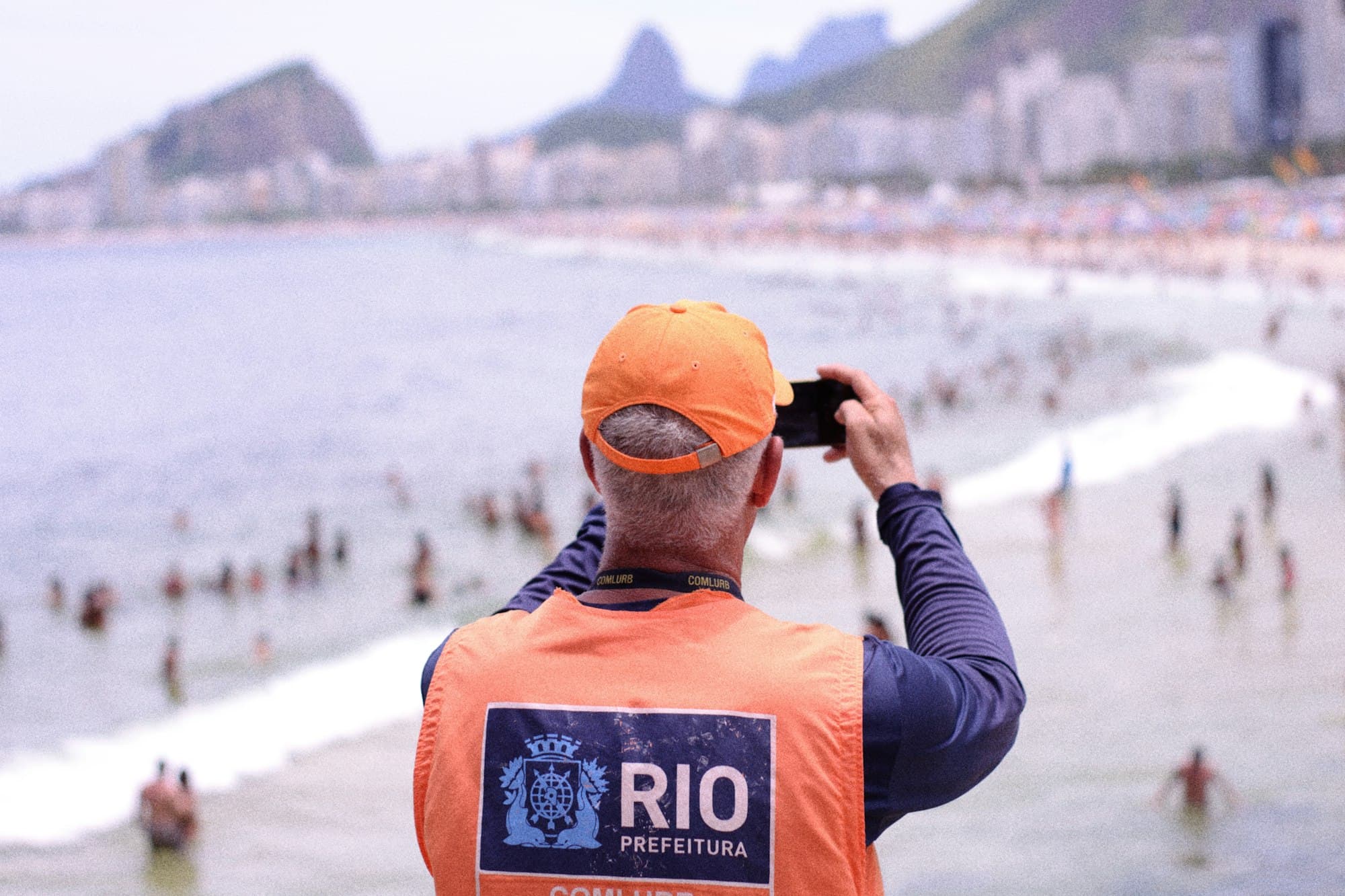 Funcionário da Comlurb fotografando a praia de Copacabana com o celular, com o Morro Dois Irmãos ao fundo