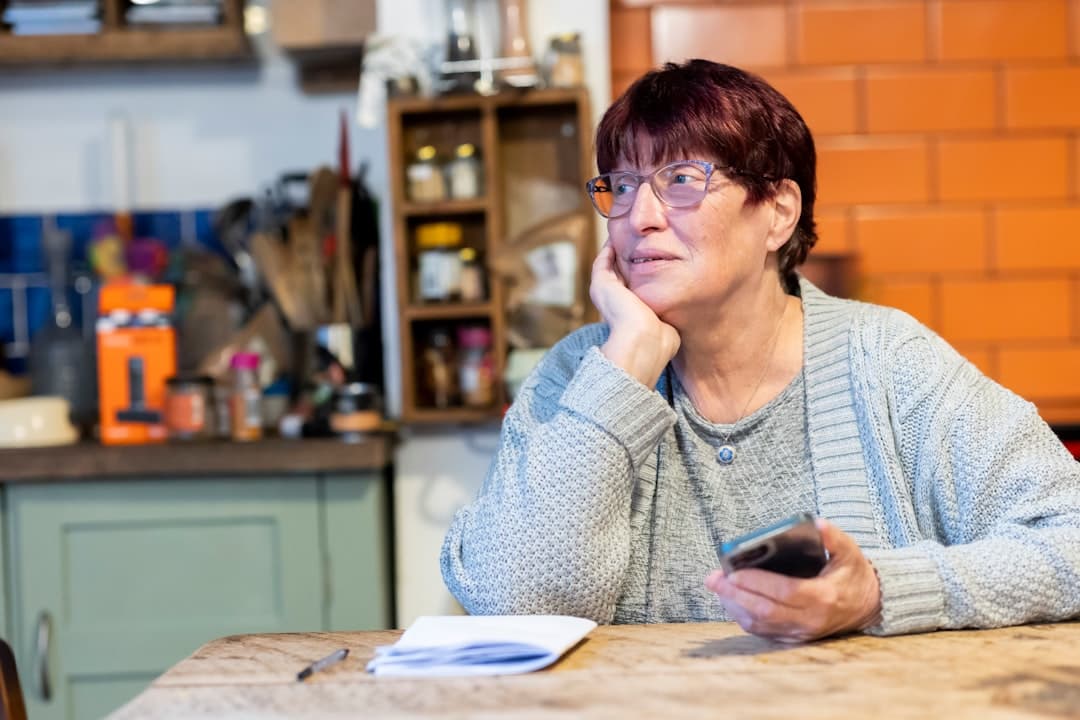 Mulher idosa usando celular sentada à mesa